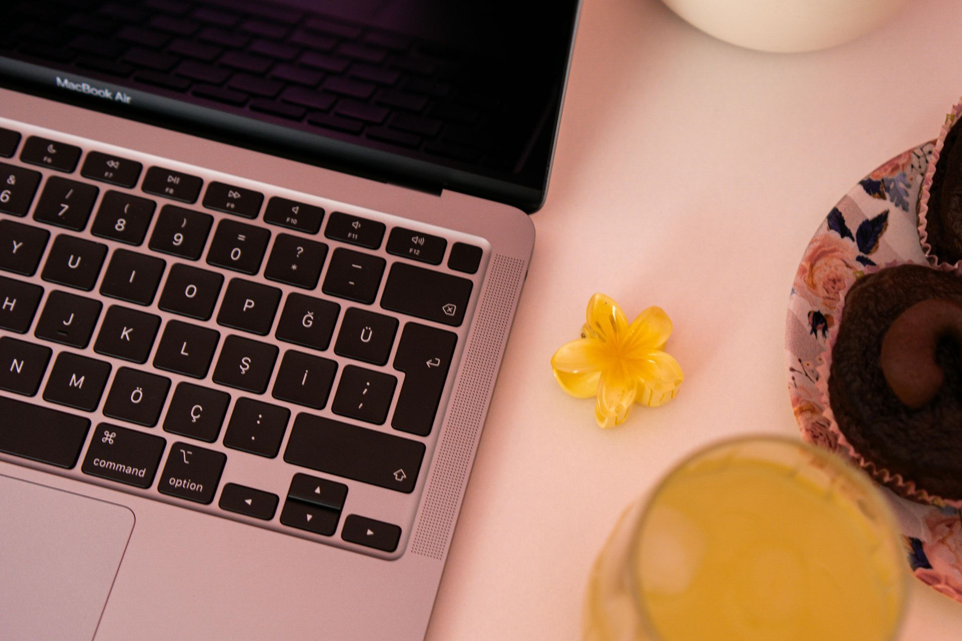 Laptop next to flower, glass of juice, and chocolate roll cakes on a plate.