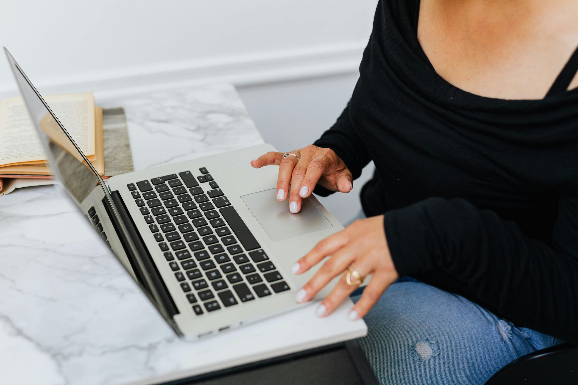 Woman working on a laptop while sitting on a bed, next to a plant.