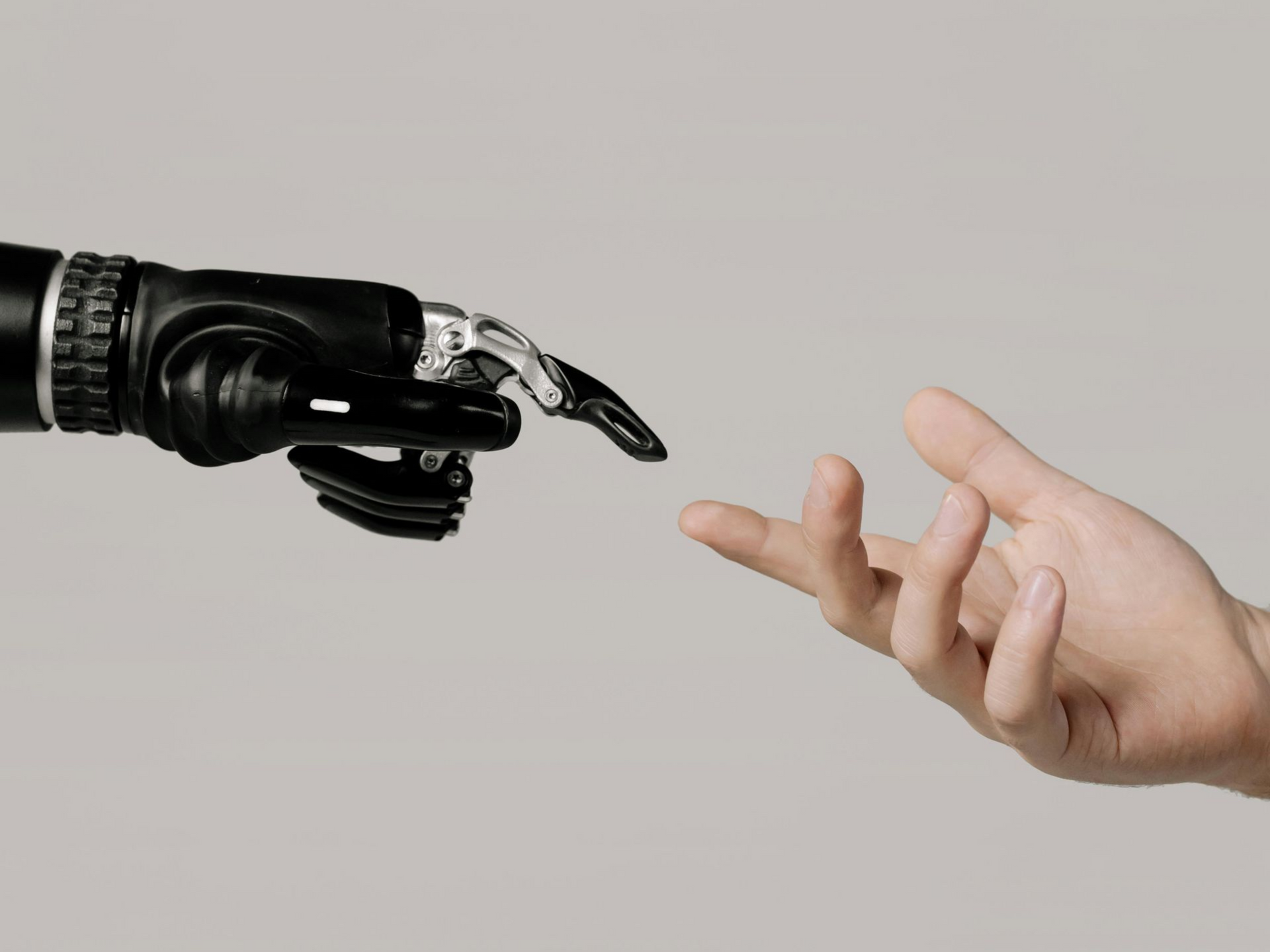 A prosthetic robotic hand reaching toward a human hand against a neutral background.