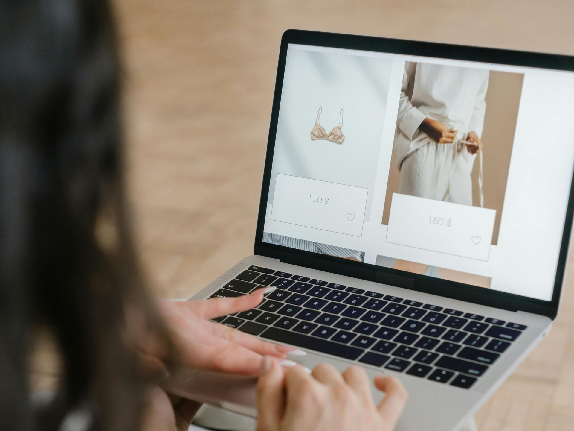 Woman browsing lingerie on a laptop; neutral tones, hands on keyboard.