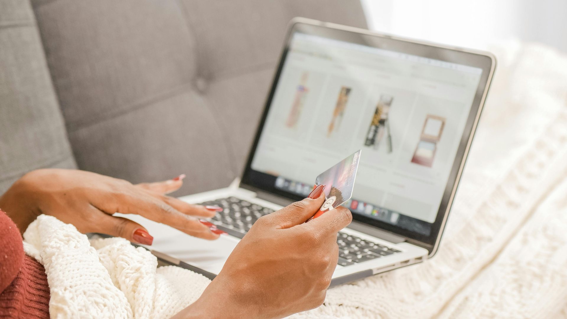 Woman shopping online on a laptop, holding a credit card, resting on a couch.