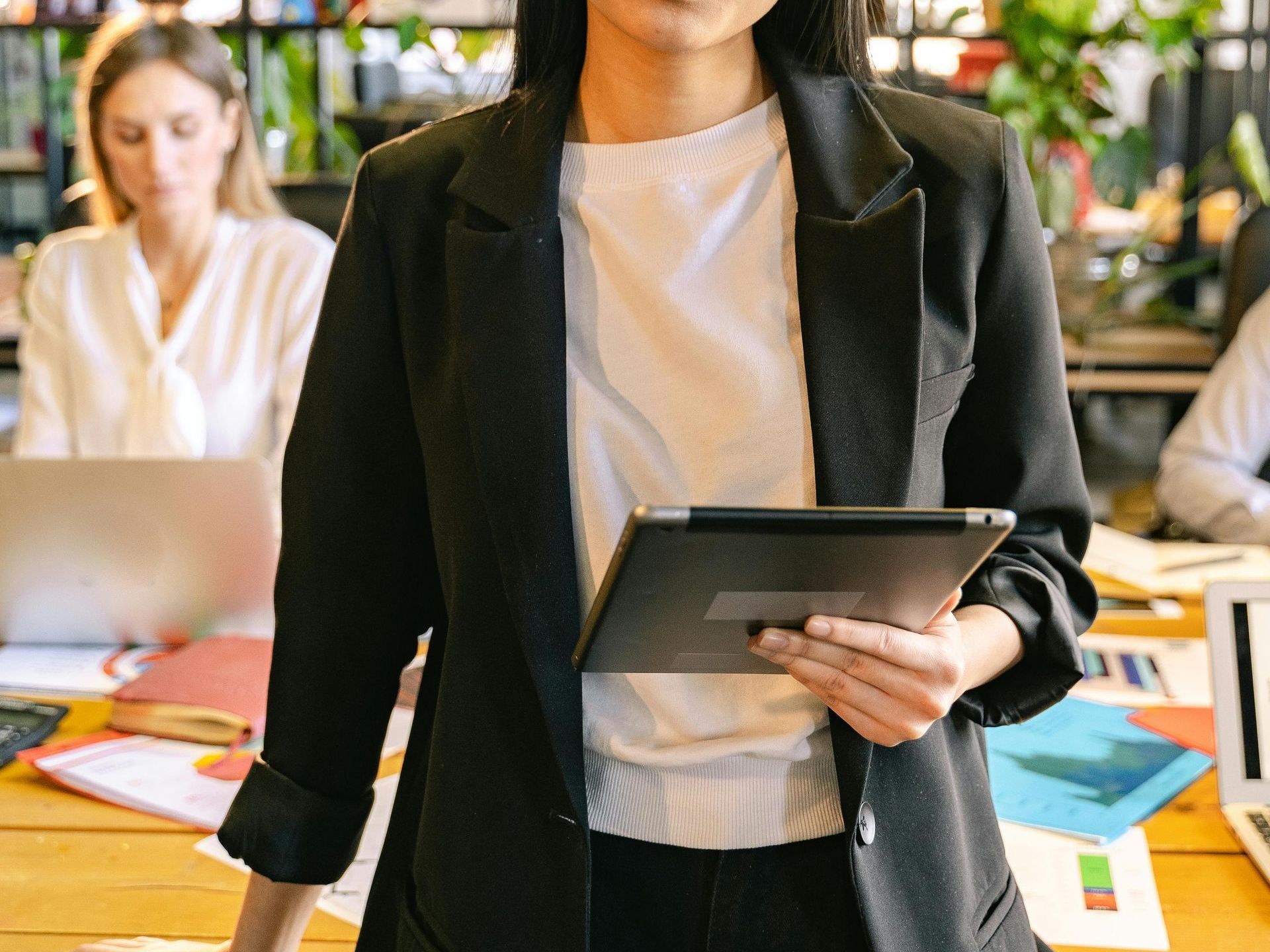 Woman in blazer holding tablet, standing in office setting.
