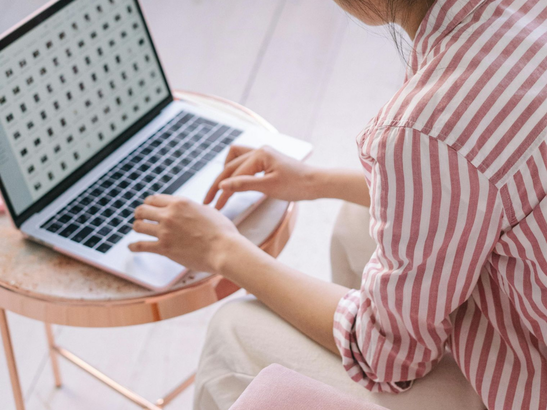 Person in striped shirt using laptop on a small table, indoors.