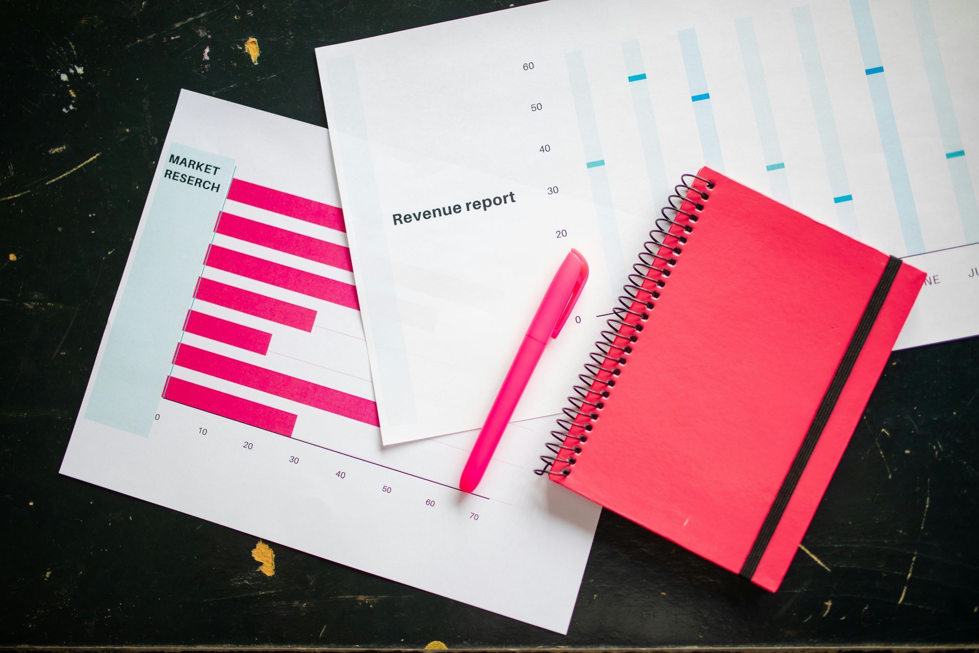 Red notepad, pen, and papers with pink and blue graphs on a black surface.