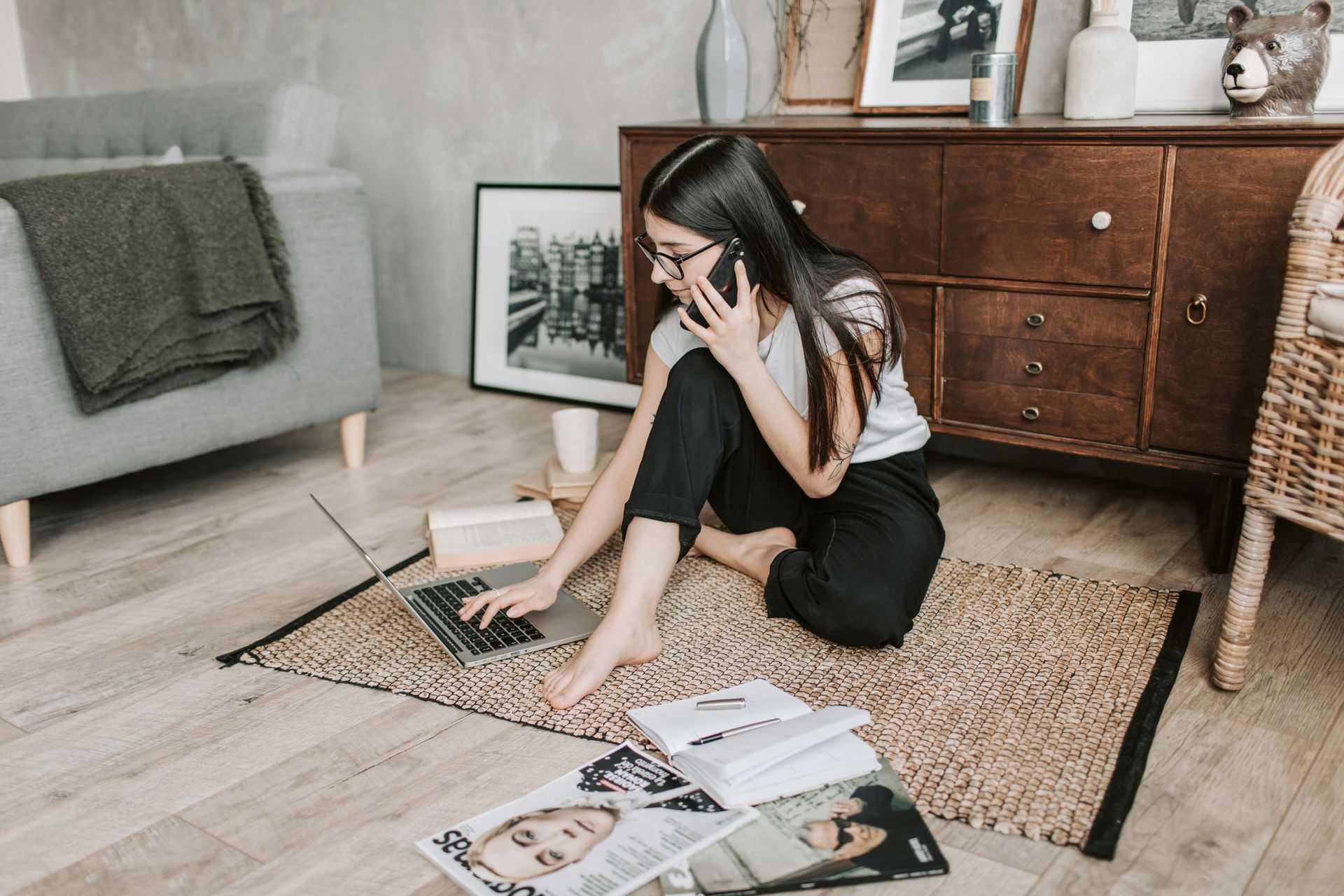 Person sitting on a rug surrounded by magazines and a laptop in a cozy living room