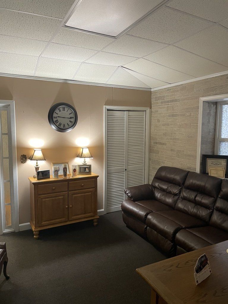 A living room with a brown couch and a clock on the wall.
