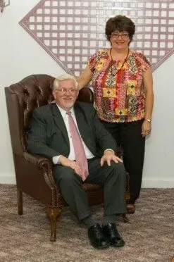 A man in a suit and tie is sitting in a chair next to a woman.