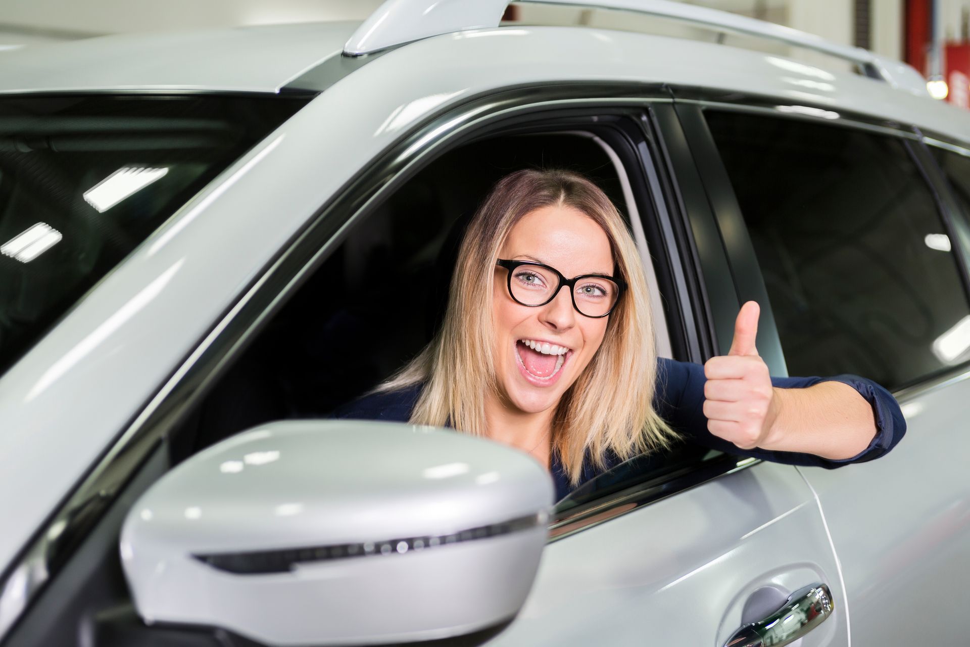 A woman is giving a thumbs up while sitting in a car.