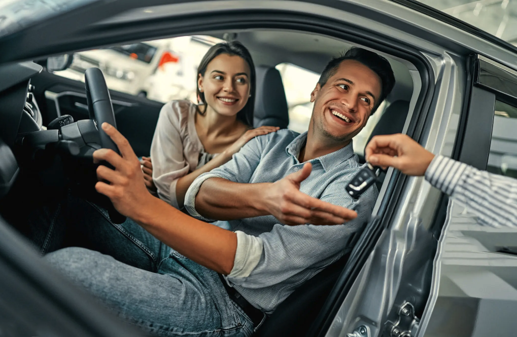 A man and a woman are sitting in a car at a car dealership.