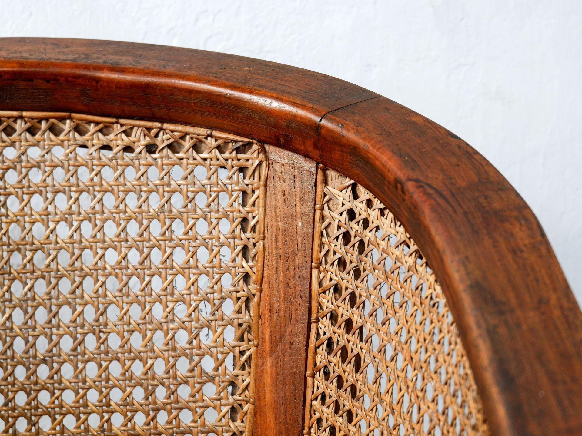 A close-up view of a dark wood chair back featuring a curved frame and light brown woven cane mesh backing.