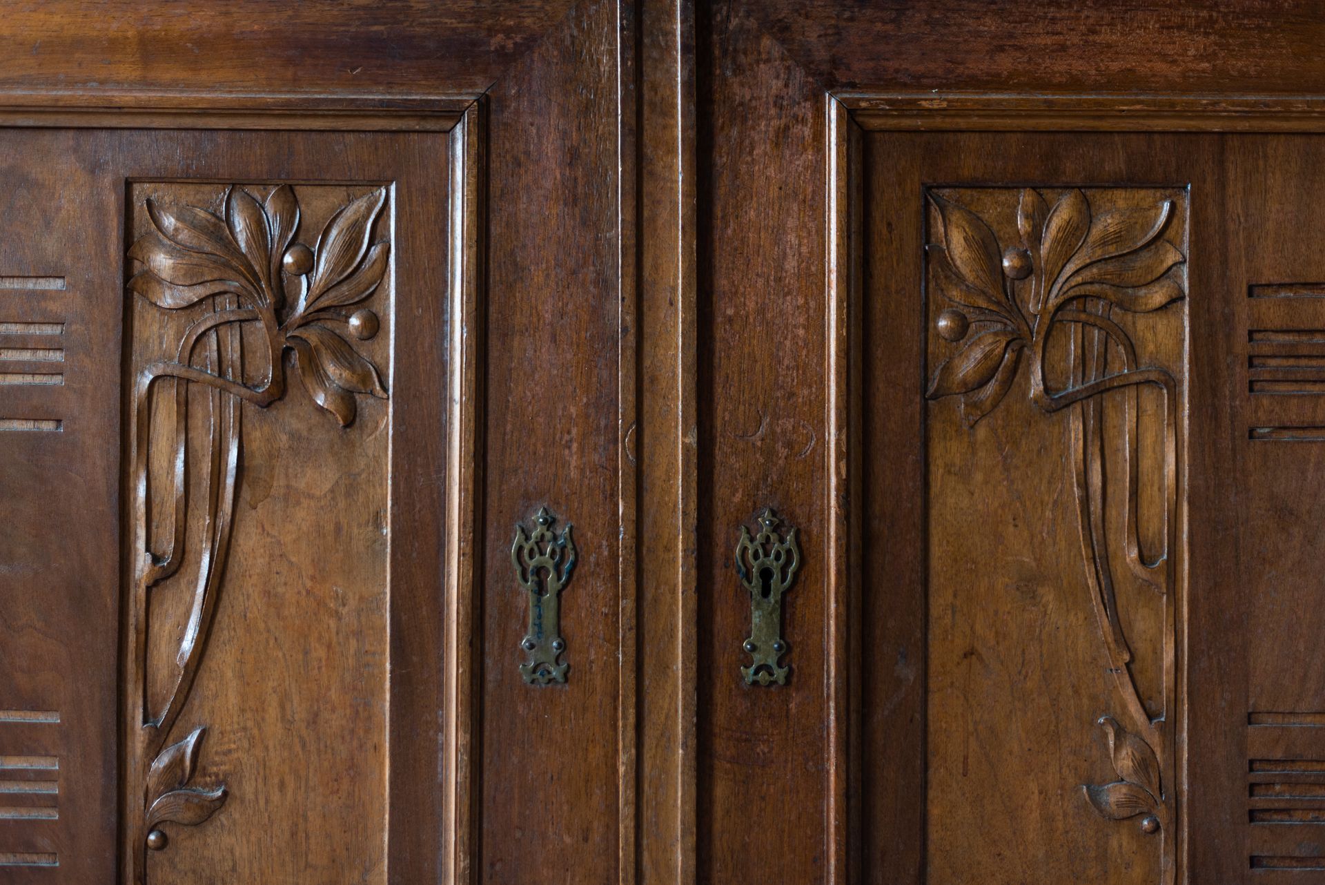 Two dark wooden cabinet doors with symmetrical floral carvings and ornate metal keyhole plates.