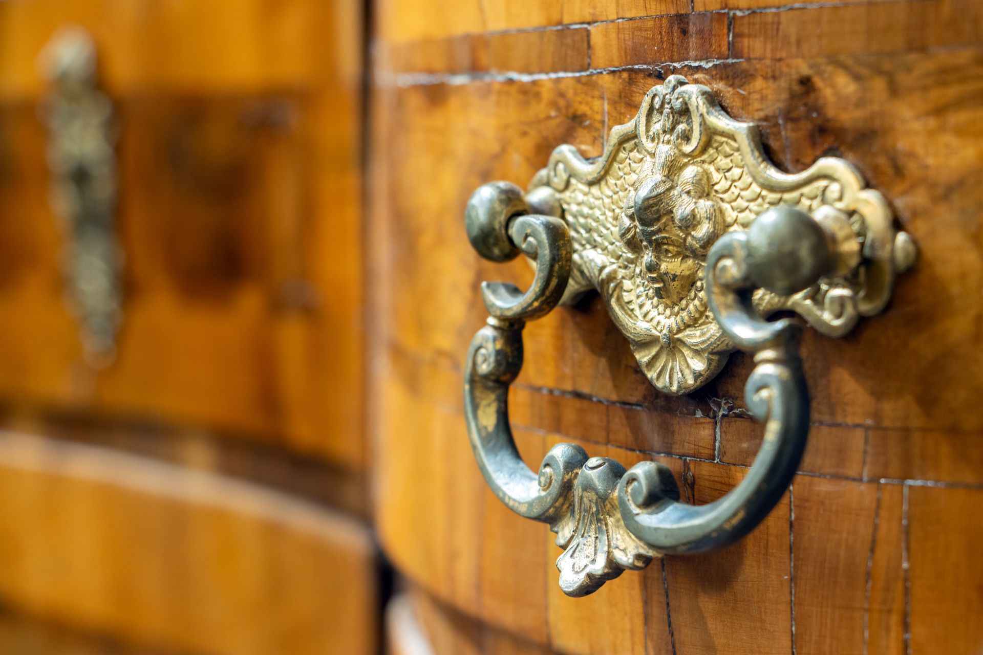 Close-up of an ornate brass drawer handle and a matching keyhole escutcheon on a polished wood cabinet.