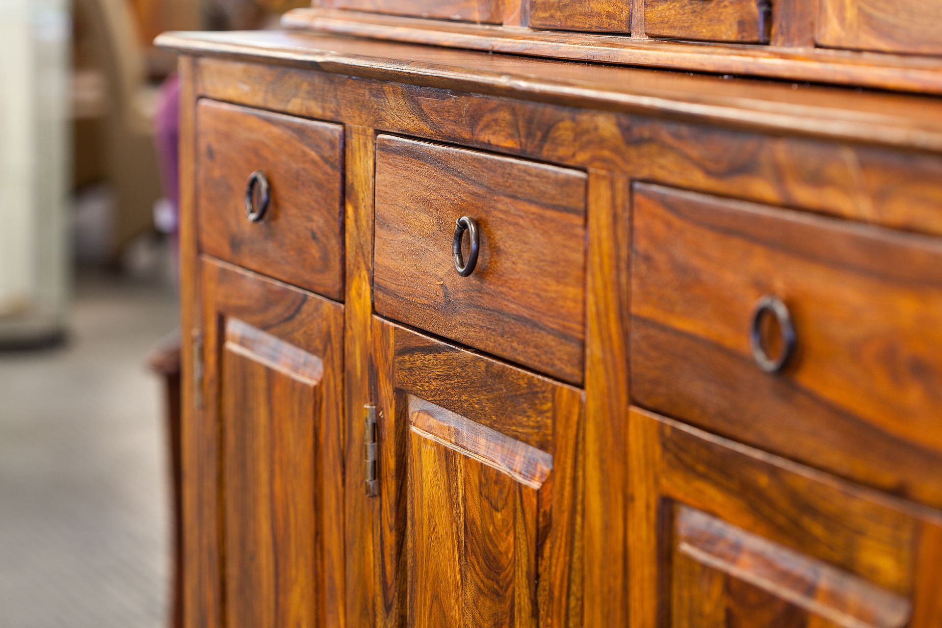 Close-up of a wooden sideboard with three drawers and matching circular metal pulls, set in a brightly lit room.