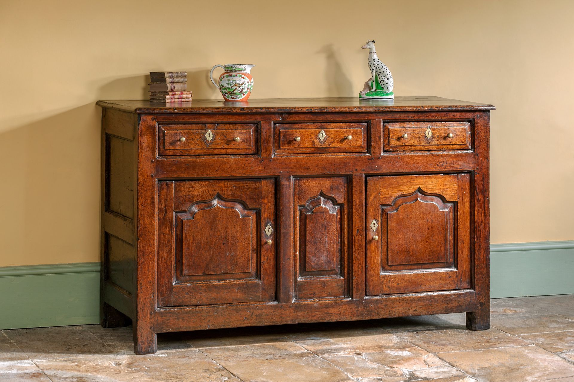 An antique dark wood sideboard with three drawers and two cabinet doors, topped with a small pitcher and a dog figurine.