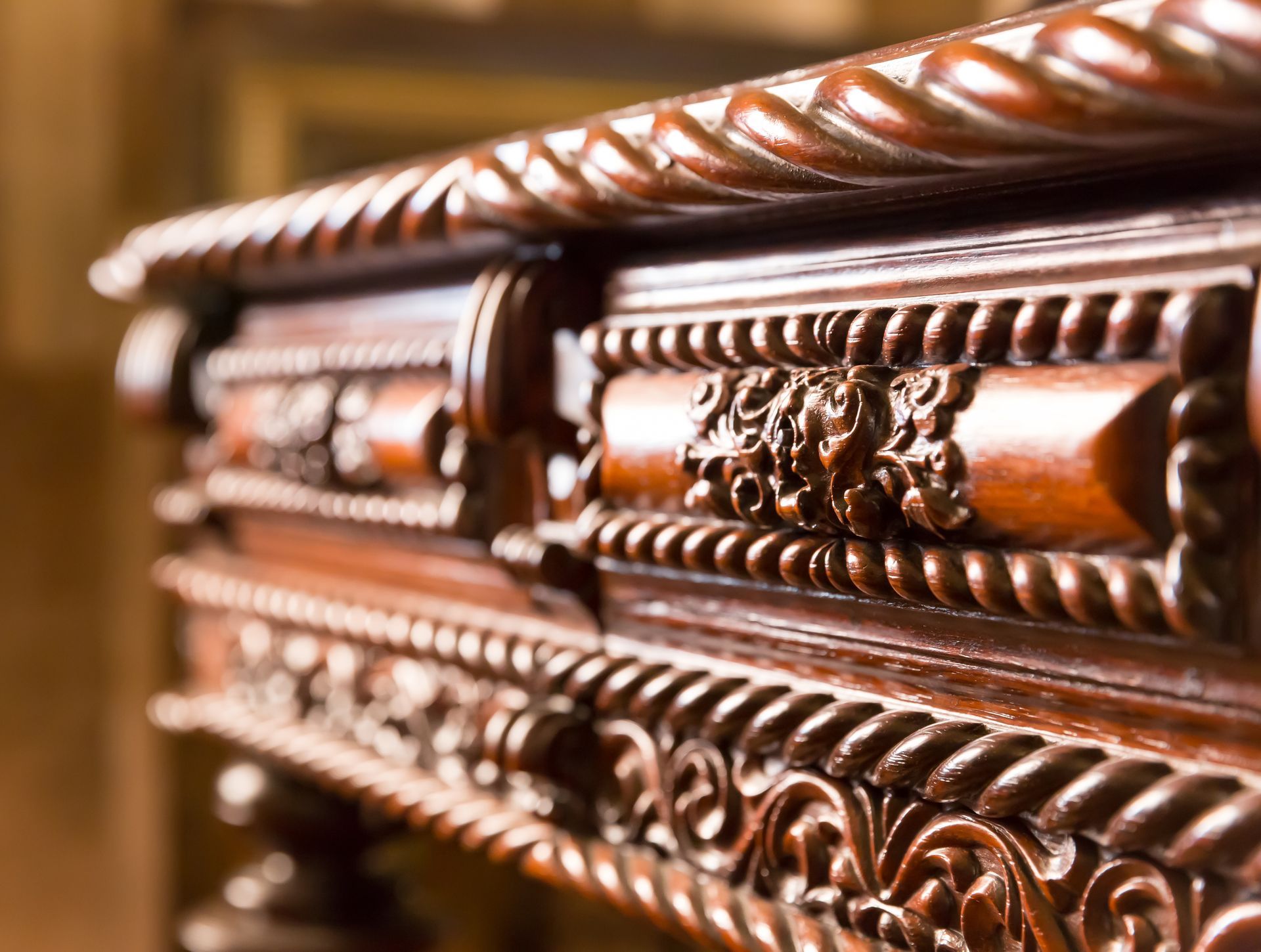 Close-up of a dark wood furniture piece featuring intricate carvings, braided rope-style trim, and floral detailing.