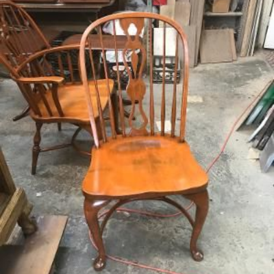 A wooden dining chair with a red cushion sits beside an ornate, carved wooden table in a dimly lit, vintage-style room.