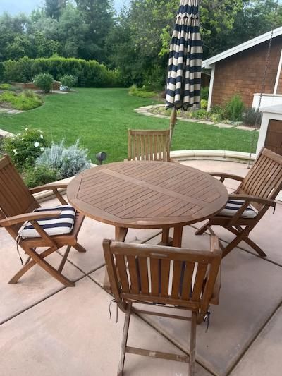 A vintage radio and a bright orange telephone sit on a wooden table next to a patterned, pink upholstered armchair.