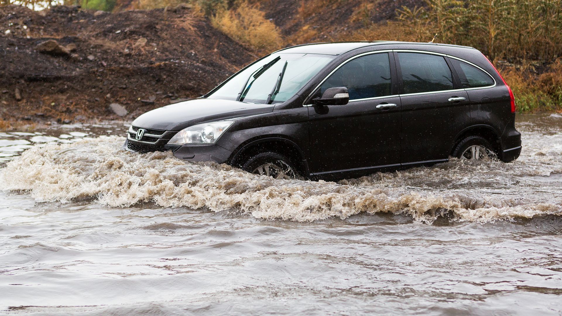 A car is driving through a flooded river.