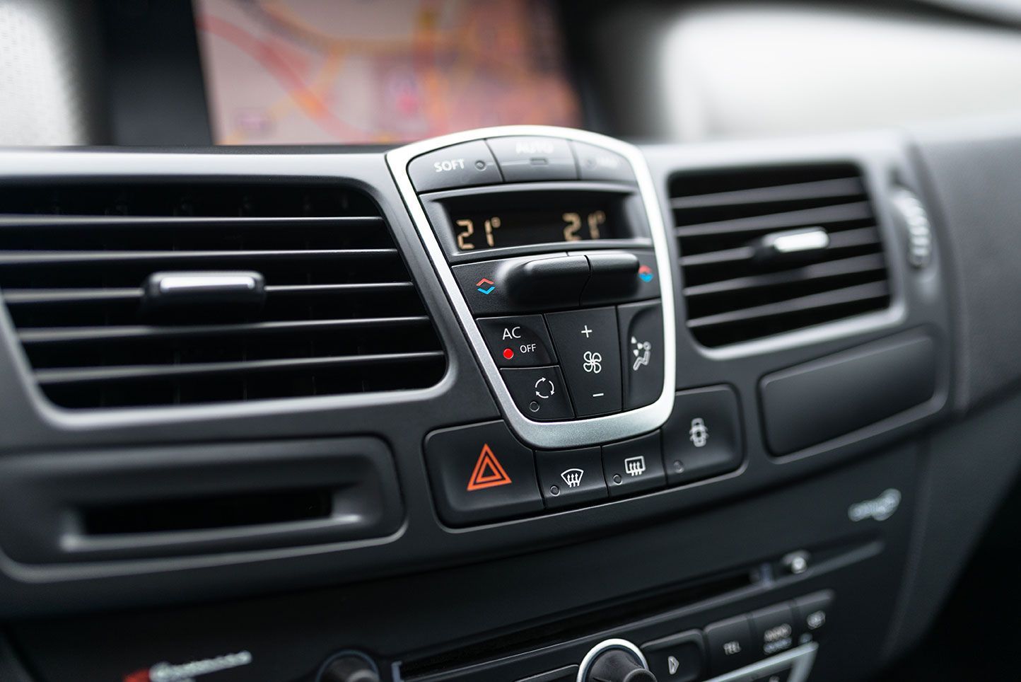 Car dashboard with climate control buttons and air vents; shows temperature displays.
