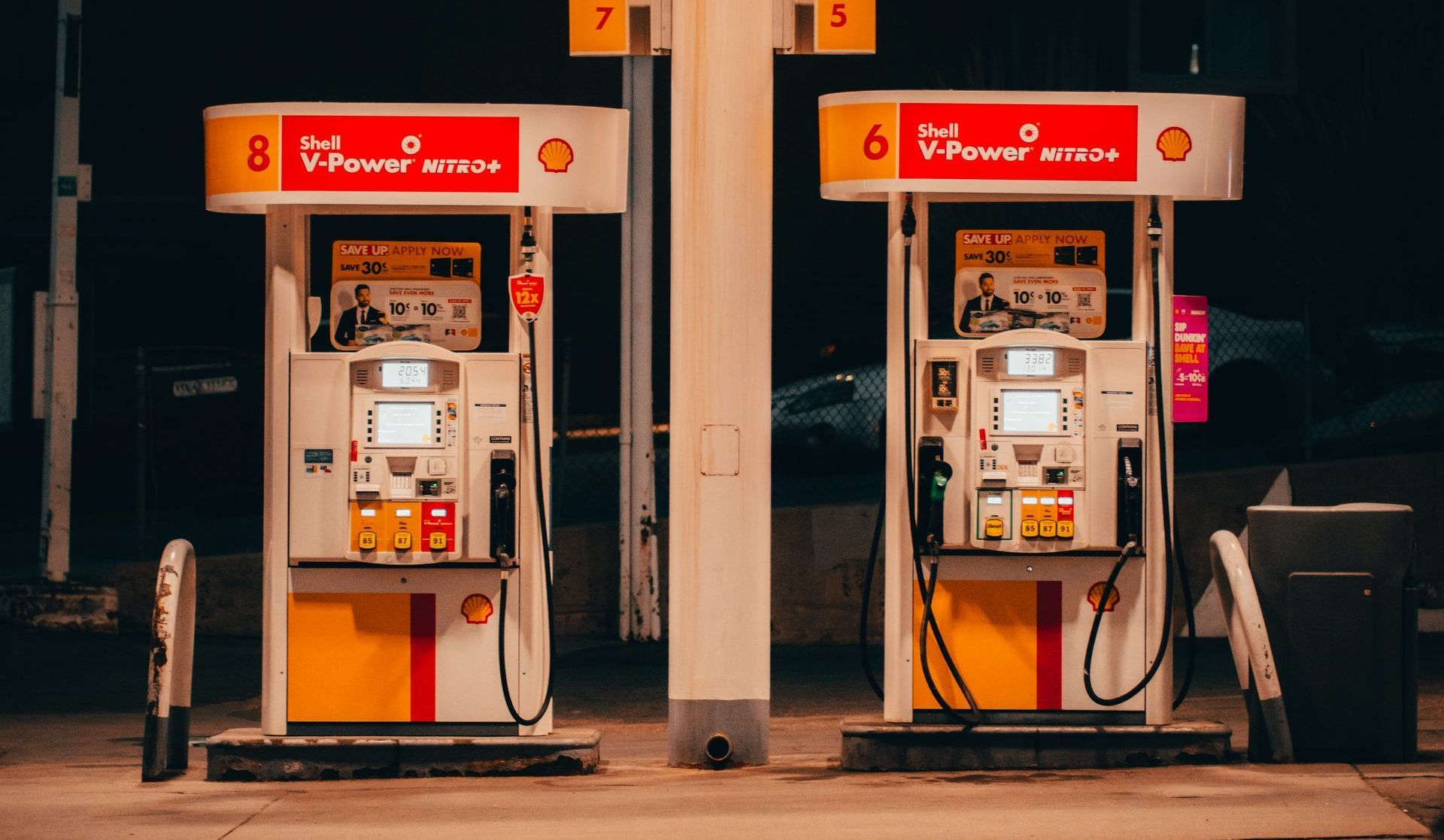 Two gas pumps are lined up in front of a gas station at night.