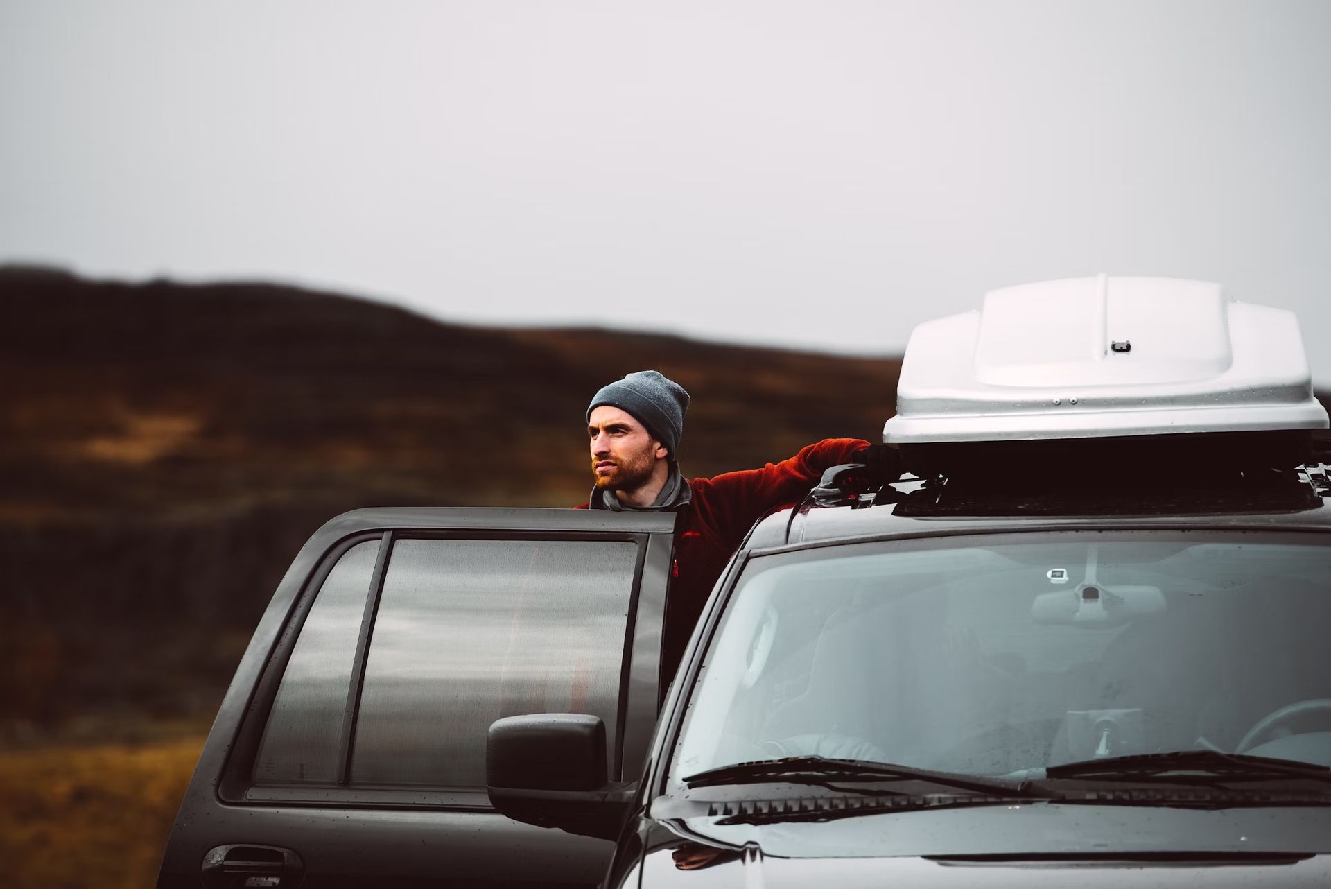 A man is standing next to a car with a roof rack on top of it.