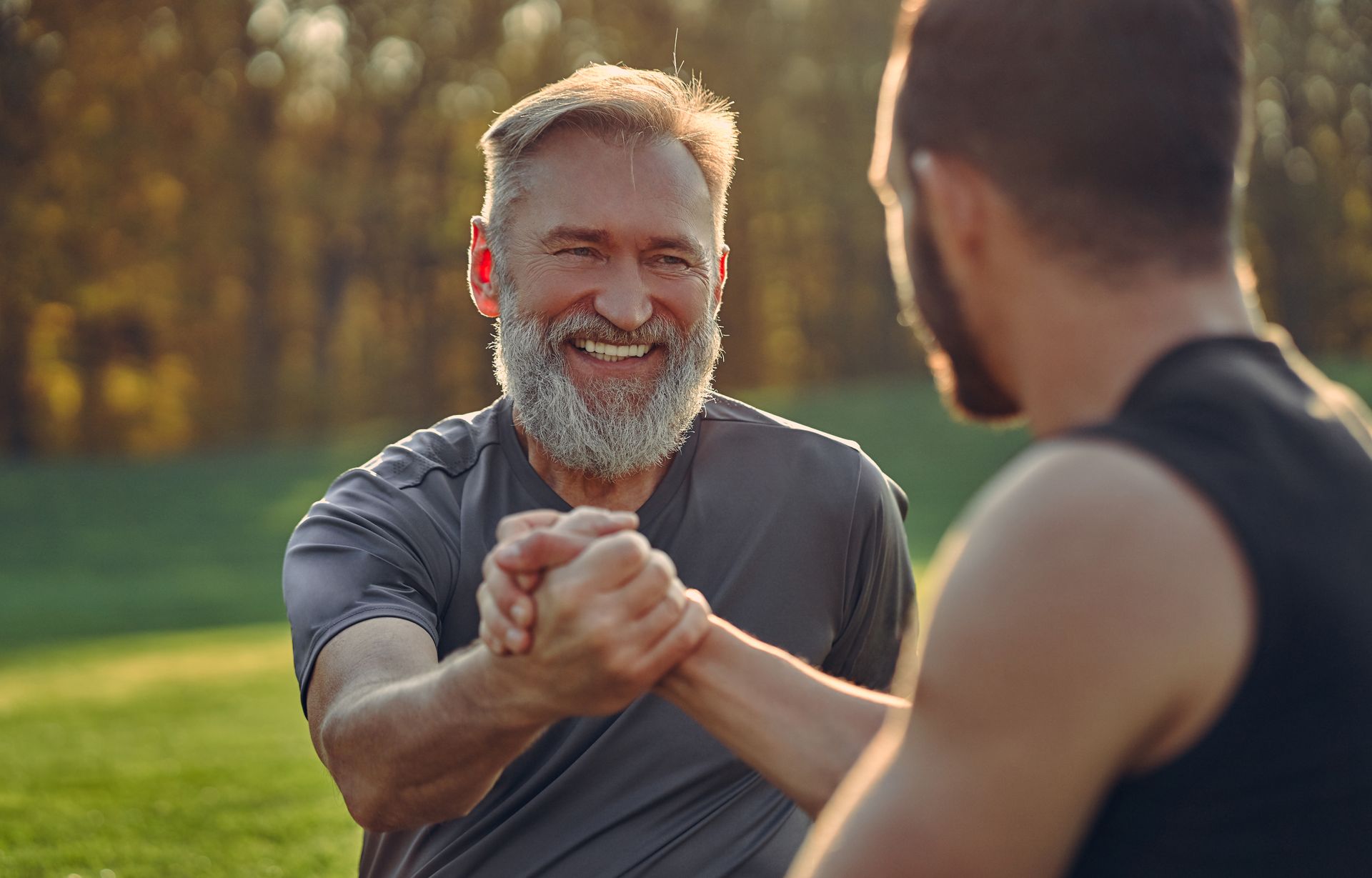 Smiling older man and younger man shaking hands outdoors.