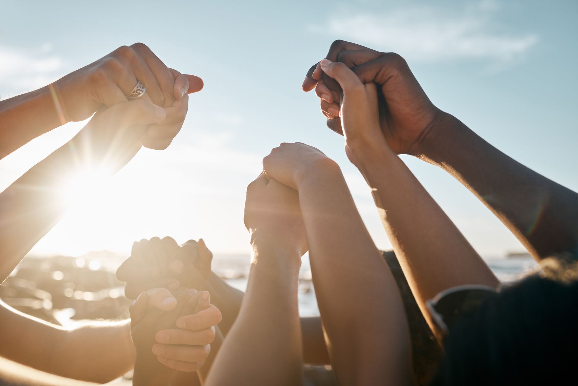 Hands of diverse people clasped together, raised toward a bright sun, representing unity and support.