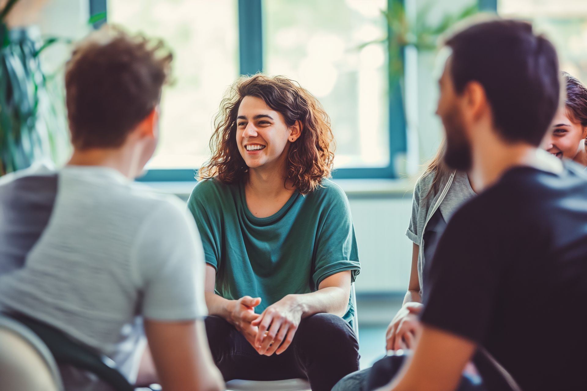 Group of people sitting in a circle, smiling and talking in a well-lit room.