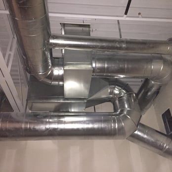 A bunch of metal aircon pipes are hanging from the ceiling of a building.