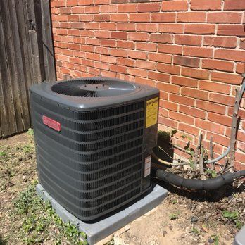 A black air conditioner is sitting next to a brick wall.