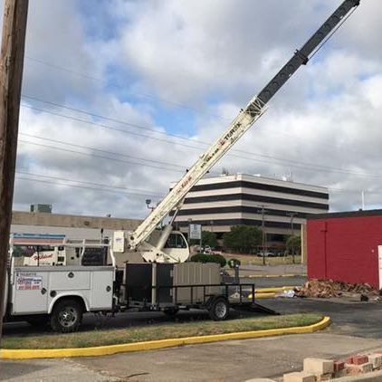 A white truck with a crane attached to it is parked in front of a red building, aircon installation.
