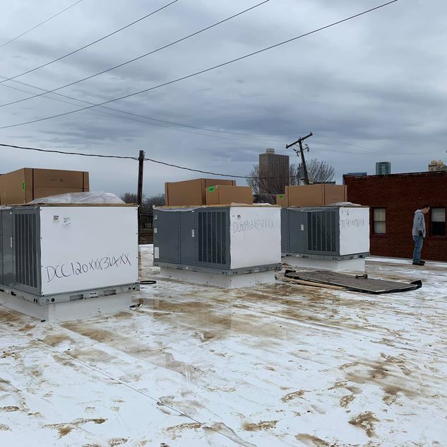 A man is standing in front of a row of air conditioners in the snow.