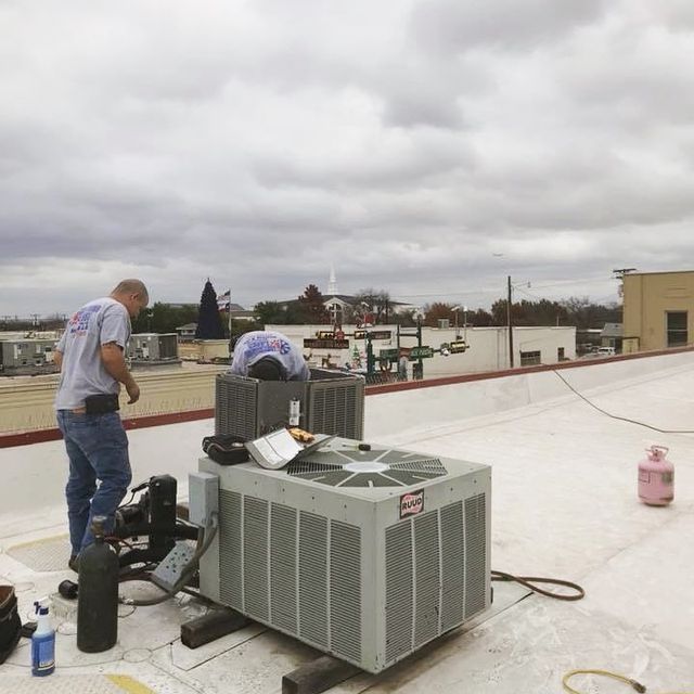 A man is working on an air conditioner on the roof of a building