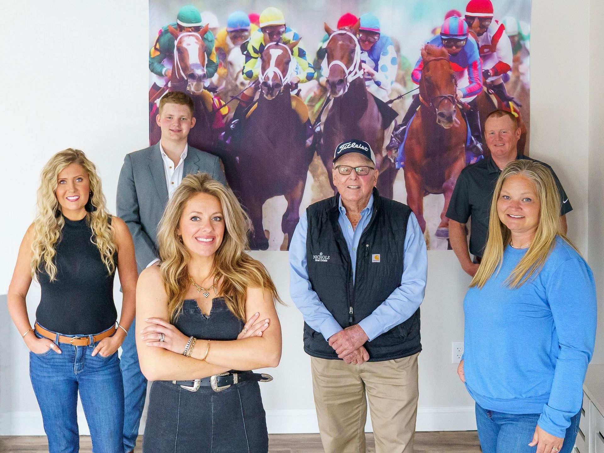 Nichols Real Estate team smiling in front of horse racing banner against a blank white wall
