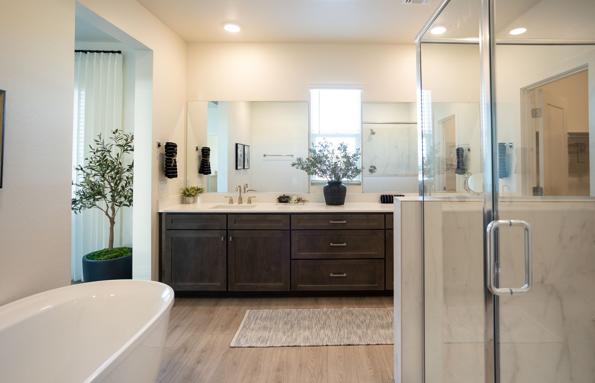 Modern bathroom with dark vanity, white tub, and glass shower door