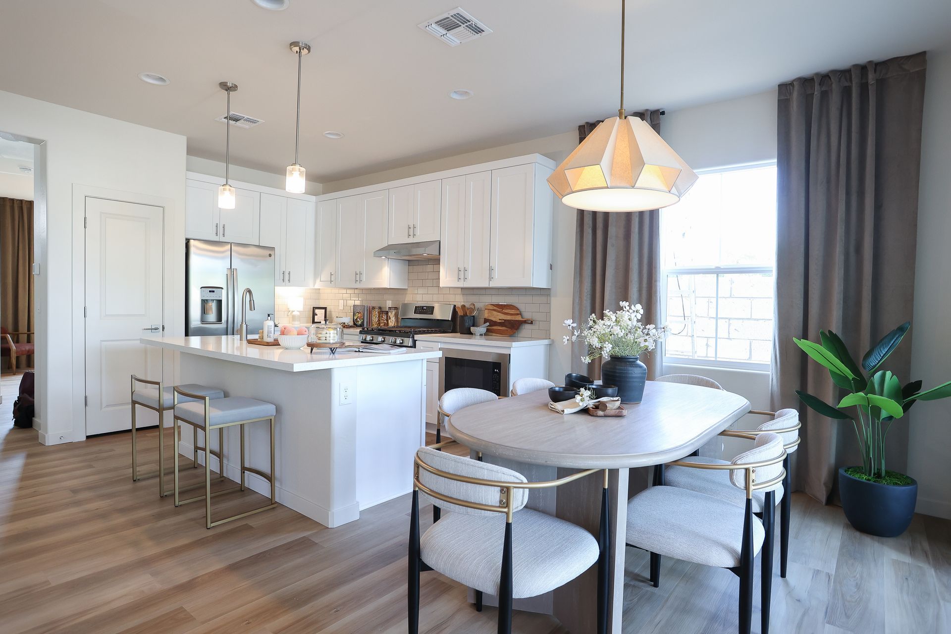 Bright modern kitchen and dining area with white cabinets, island stools, round table, and large window curtains