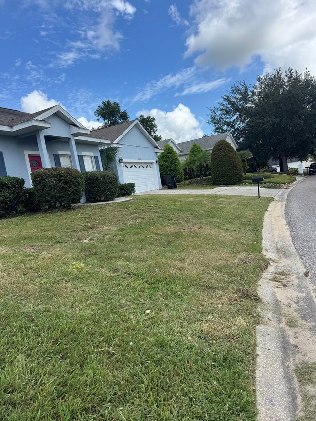 Blue houses with a green lawn under a partly cloudy sky. Concrete sidewalk on right.