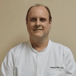 A man in a white coat is smiling for the camera.