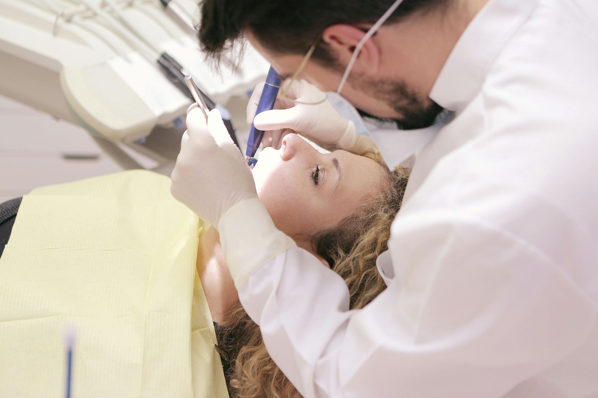 A dentist is examining a woman 's teeth in a dental chair.