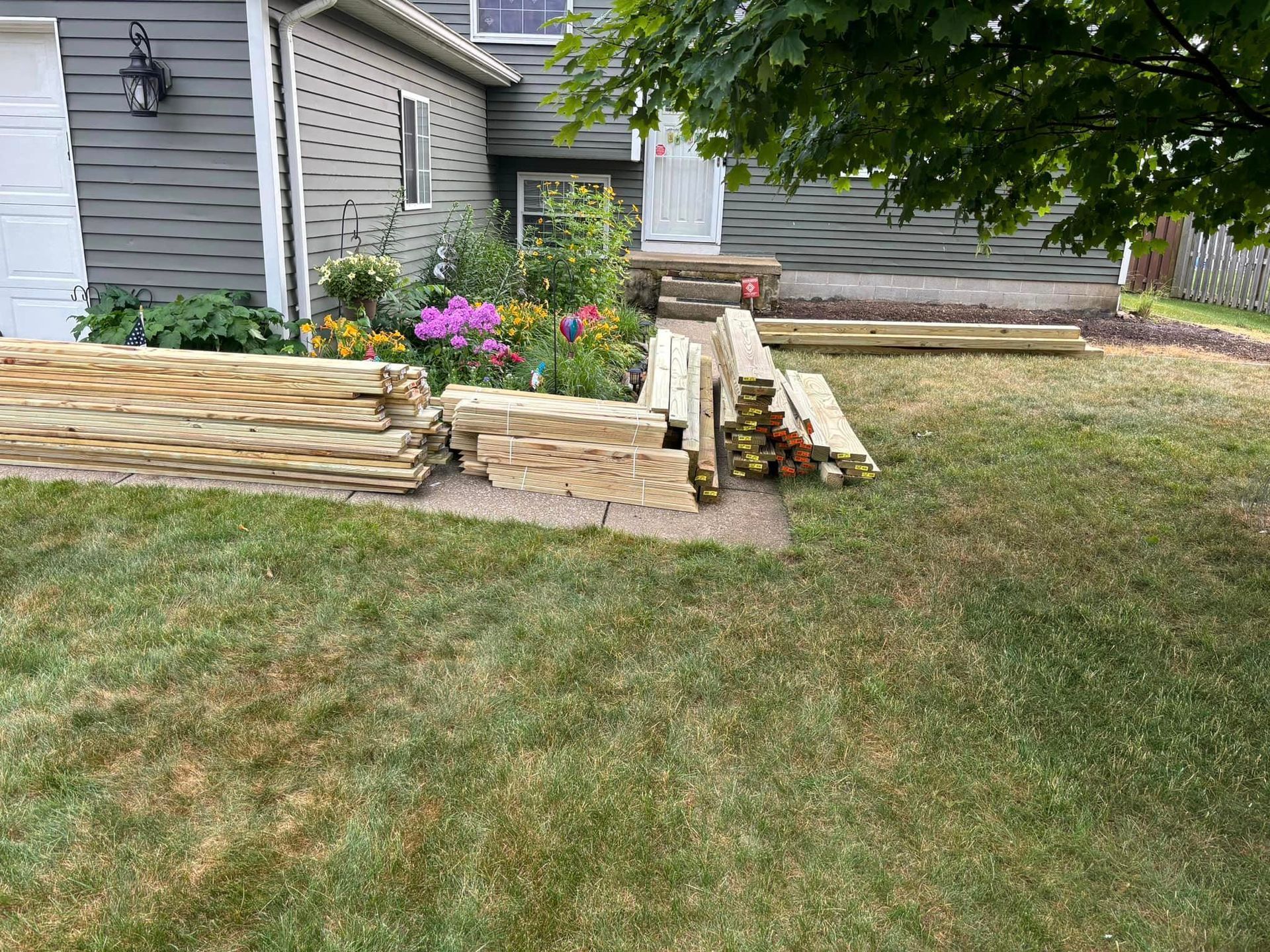 A pile of wood is sitting in the grass in front of a house.