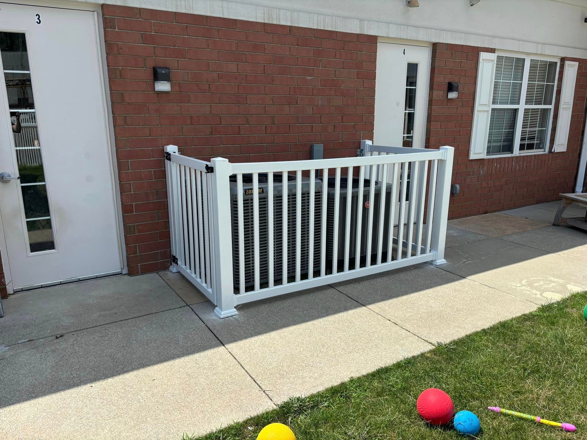 A white fence is sitting in front of a brick building.