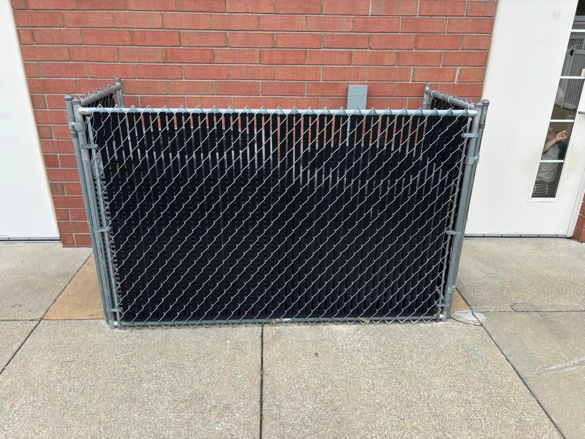 A chain link fence is sitting on a sidewalk in front of a brick building.