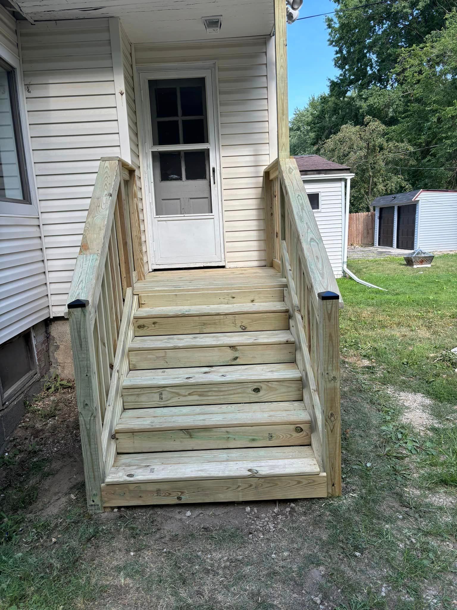 A wooden deck with stairs leading up to the front door of a house.