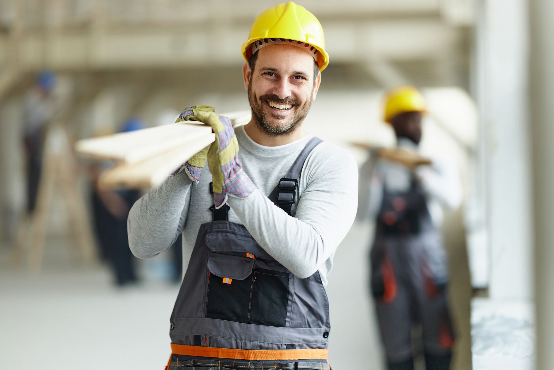 Happy male general contractor carrying wood plank at construction site.