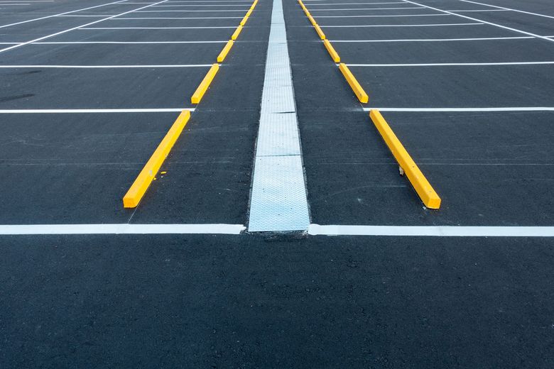 Empty parking lot with yellow parking stops, white lines, and a central dividing line.