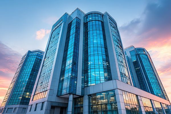A low-angle view of three modern, interconnected glass-facade office buildings against a sunset sky.