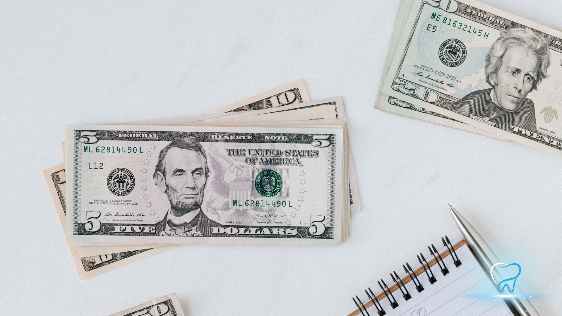 Cash money, $5 and $20 bills, a notepad, and a pen on a white surface.