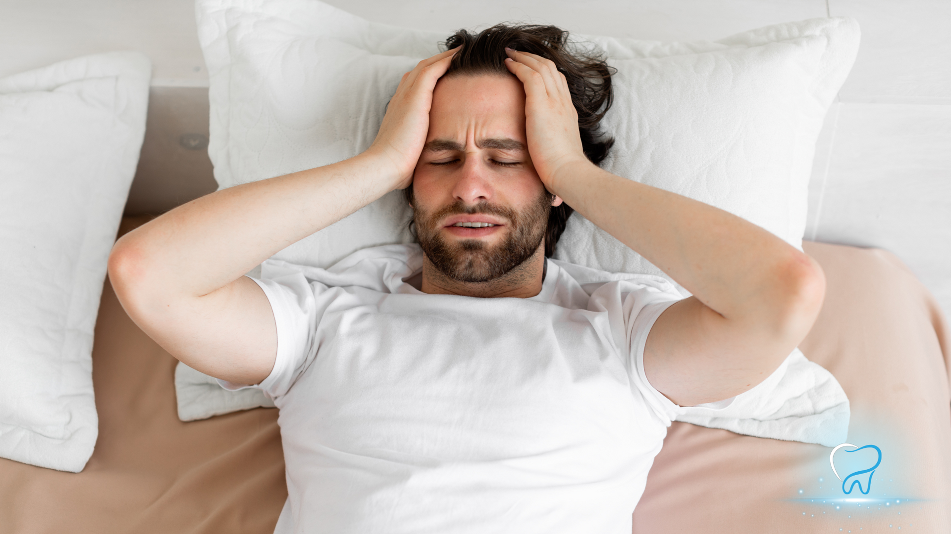 A man is laying in bed with his hands on his head.