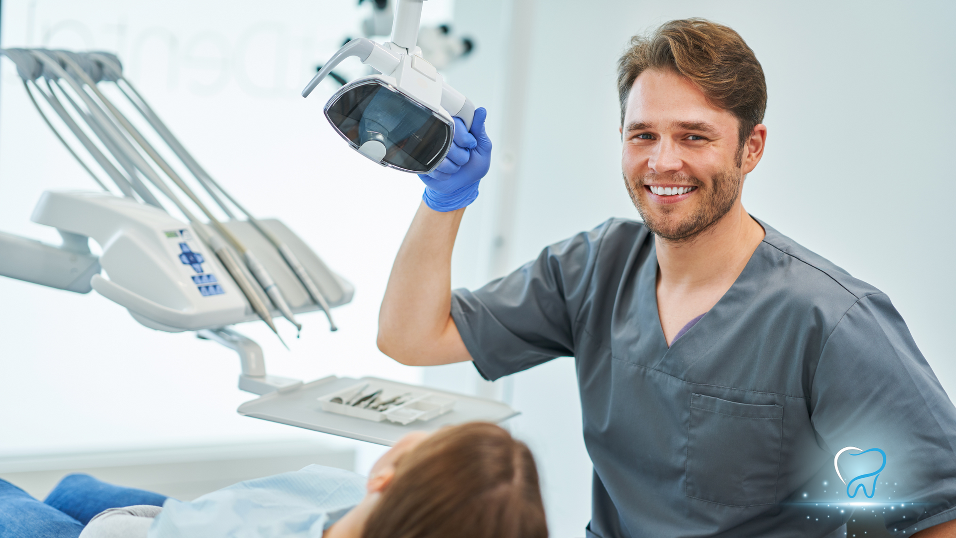 A dentist is smiling while standing next to a patient in a dental chair.
