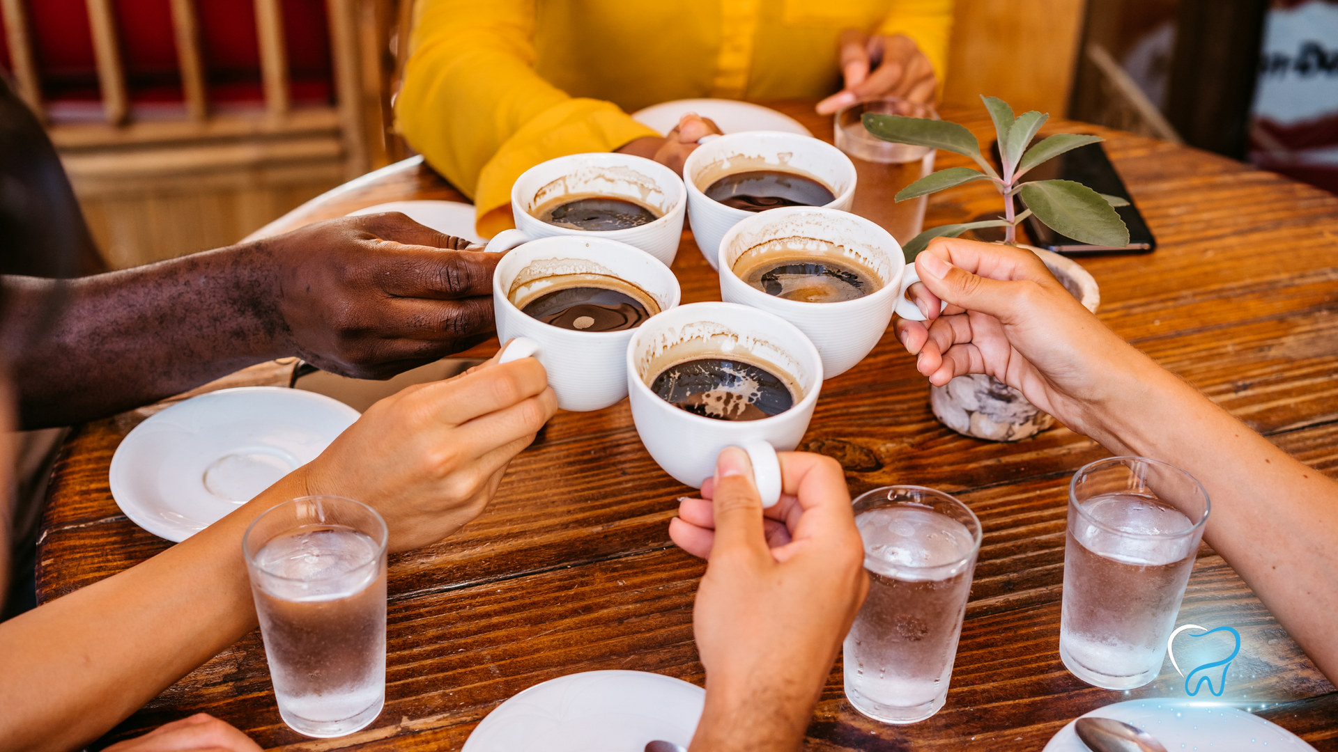 A group of people are sitting at a table holding cups of coffee and glasses of water.